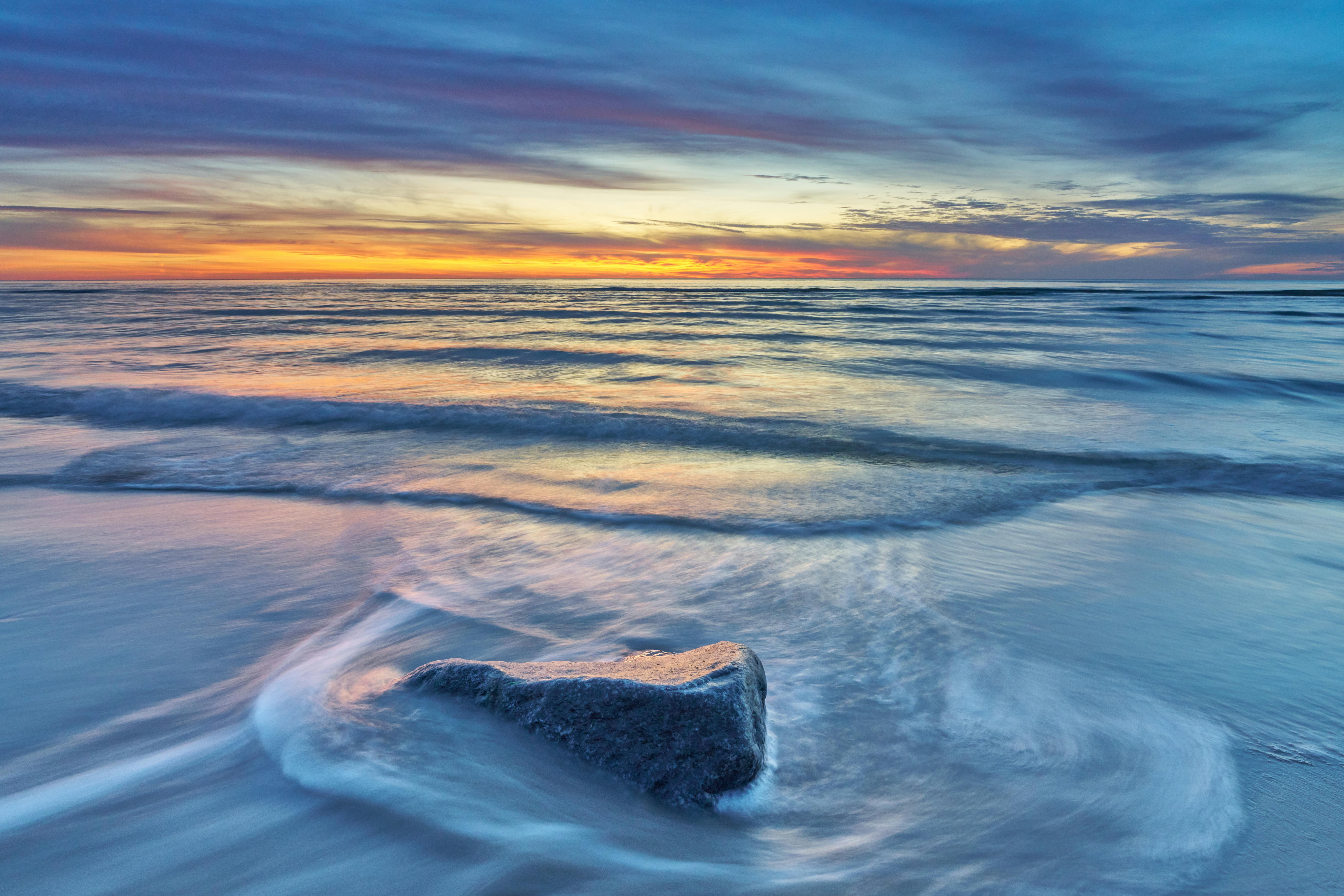 Stone in sandy beach at sunrise symbolizing challenges being softened by healing waves.
